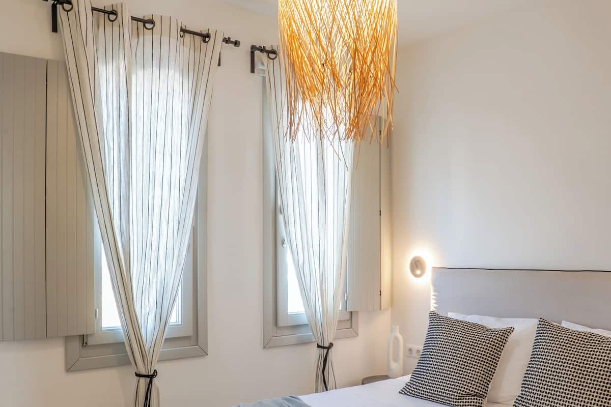 A bedroom with a large bed, a hanging light fixture, and curtains on the windows.