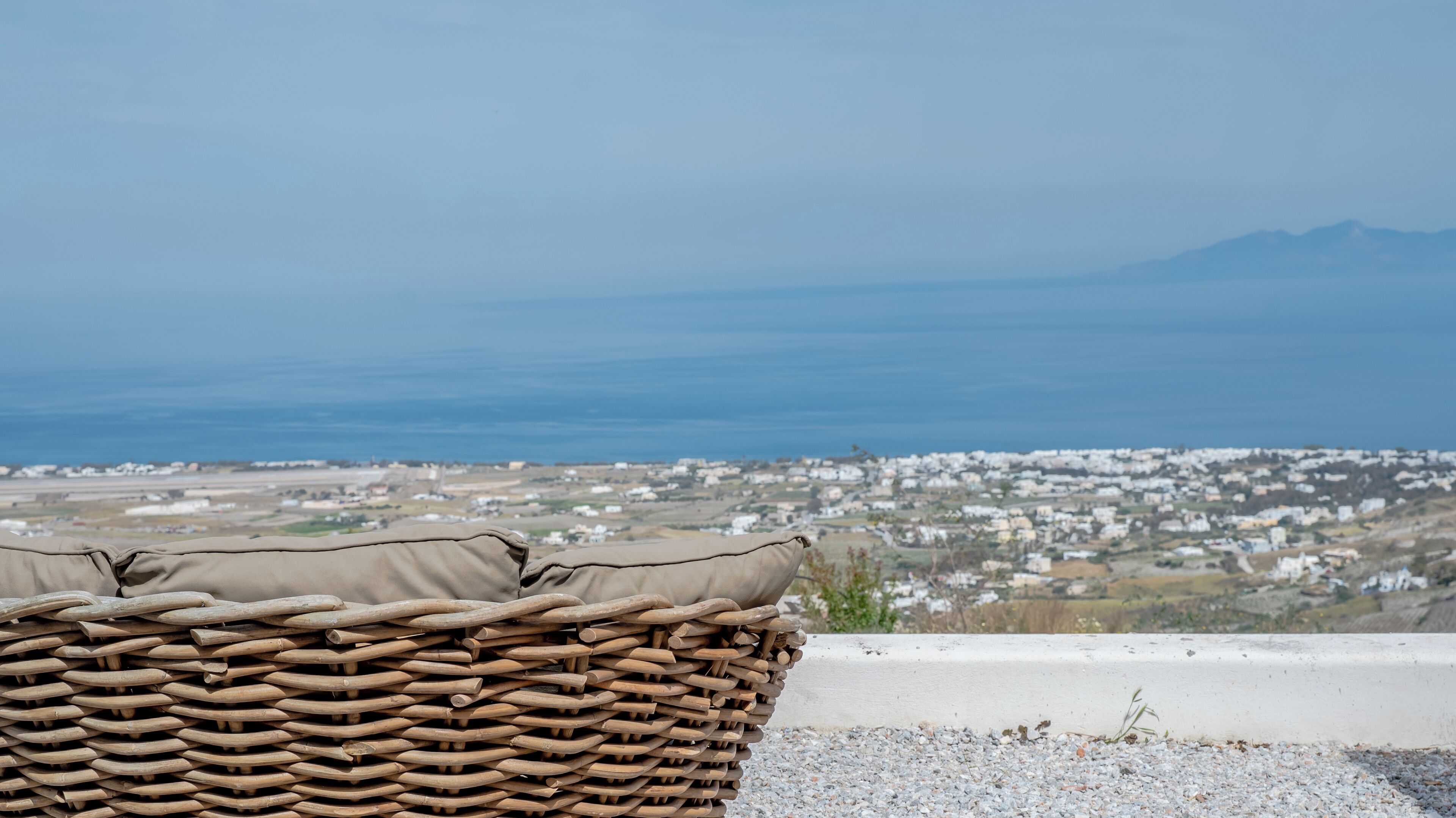 Una silla de mimbre con cojín, con vista a un pueblo costero y al mar.
