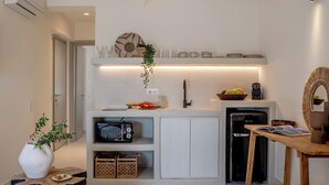 A modern living room with a large woven pendant light, a kitchen area with white cabinets, and a dining table with a bowl of fruit. - Ico Santorini (Santorini)