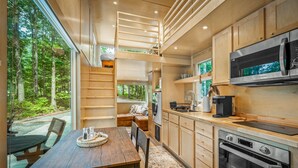 A modern kitchen with wooden cabinets, stainless steel appliances, and a dining area with a wooden table and chairs. - Boho Bungalow-unique & cozy tiny home (Mentone)