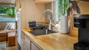 A compact kitchen with a sink, a coffee maker, and a window with a view of greenery. - Boho Bungalow-unique & cozy tiny home (Mentone)