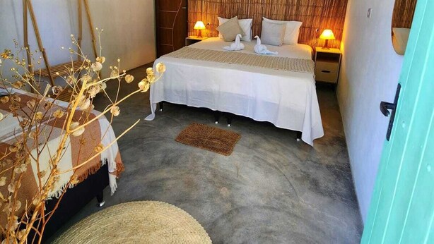 A bedroom with a bed, two bedside tables, a hanging light fixture, a door, and a wall-mounted air conditioner.