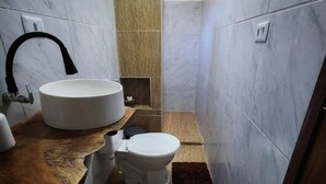 A bathroom with a round sink, a toilet, a towel rack, and a shower area.