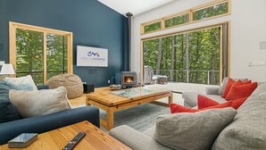 A modern living room with a fireplace, large windows, and a sign for Carolinamornings. - Secluded 3BR home on 30 acres near Green River Gorge with hot tub & trails (Saluda)