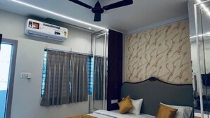 A modern bedroom with a bed, ceiling fan, air conditioning unit, and a patterned wall. - Hotel Shivngan (Ujjain)