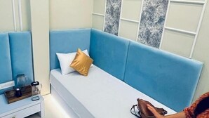 A modern room with a blue sofa, a white bedside table, and a patterned wall. - Hotel Shivngan (Ujjain)