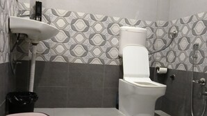 A bathroom with a toilet, bidet, and a small trash bin. - Hotel Shivngan (Ujjain)