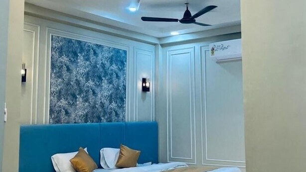 A modern hotel room with a central bed, a smaller bed, a ceiling fan, and a decorative wall. - Hotel Shivngan (Ujjain)