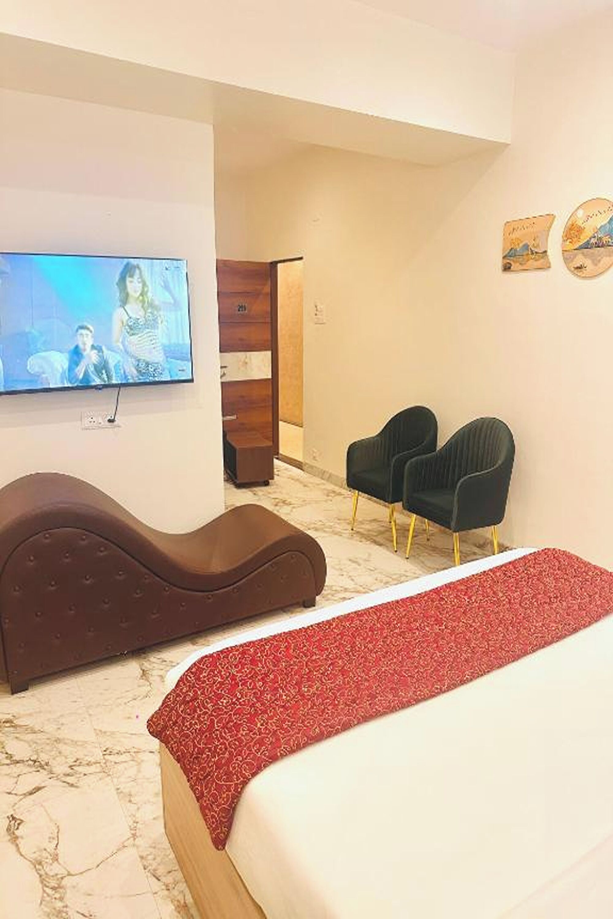 Una camera d'albergo con un letto grande, una TV a parete, due poltrone e un mobiletto in legno.