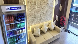 A hotel reception area with a marble wall, a beige sofa, and a 'Blue Star' refrigerator stocked with beverages. - Hotel The Ceremony (Bhiwandi)