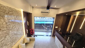 A hotel reception area with a marble wall, a sofa, a reception desk, and a view of the outside. - Hotel The Ceremony (Bhiwandi)