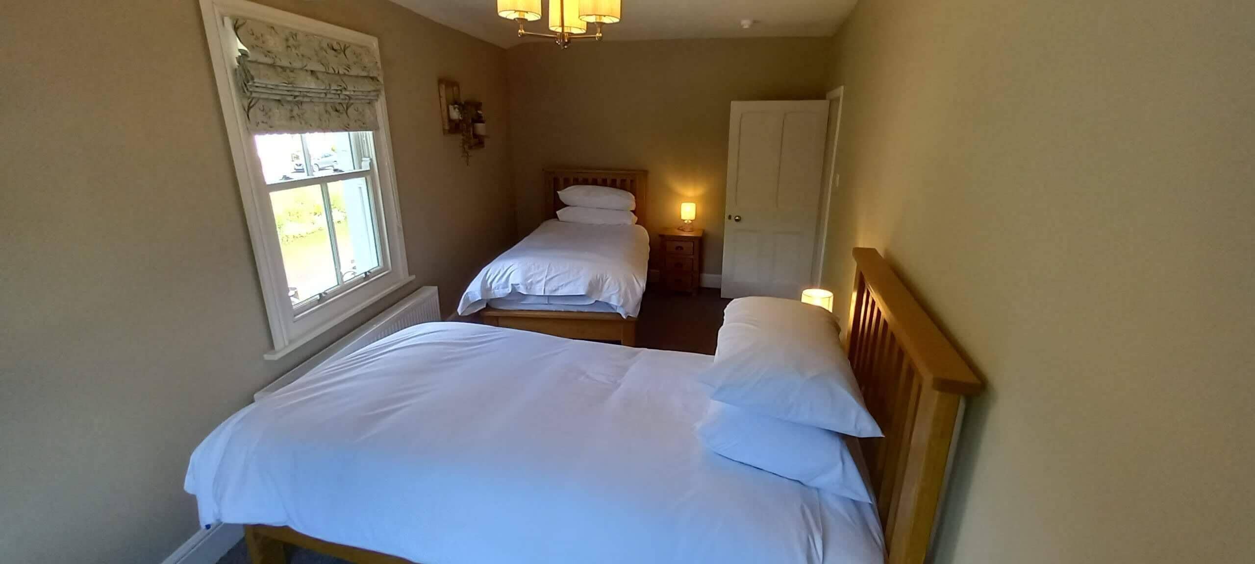 A bedroom with two single beds, a window with a view, a door, and a nightstand with a lamp.