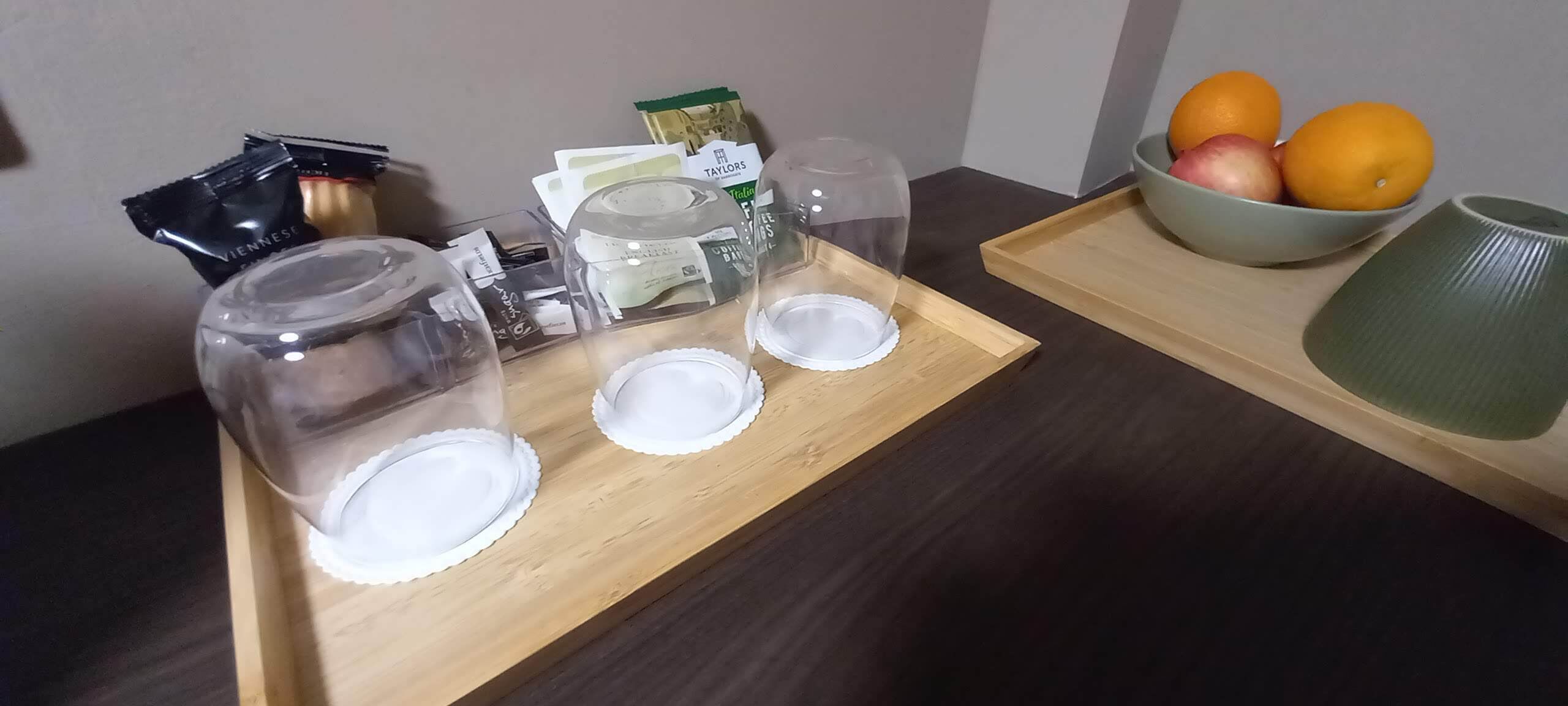 Un plateau en bois sur lequel sont disposés trois bocaux en verre transparent, un récipient transparent et un bol de fruits.