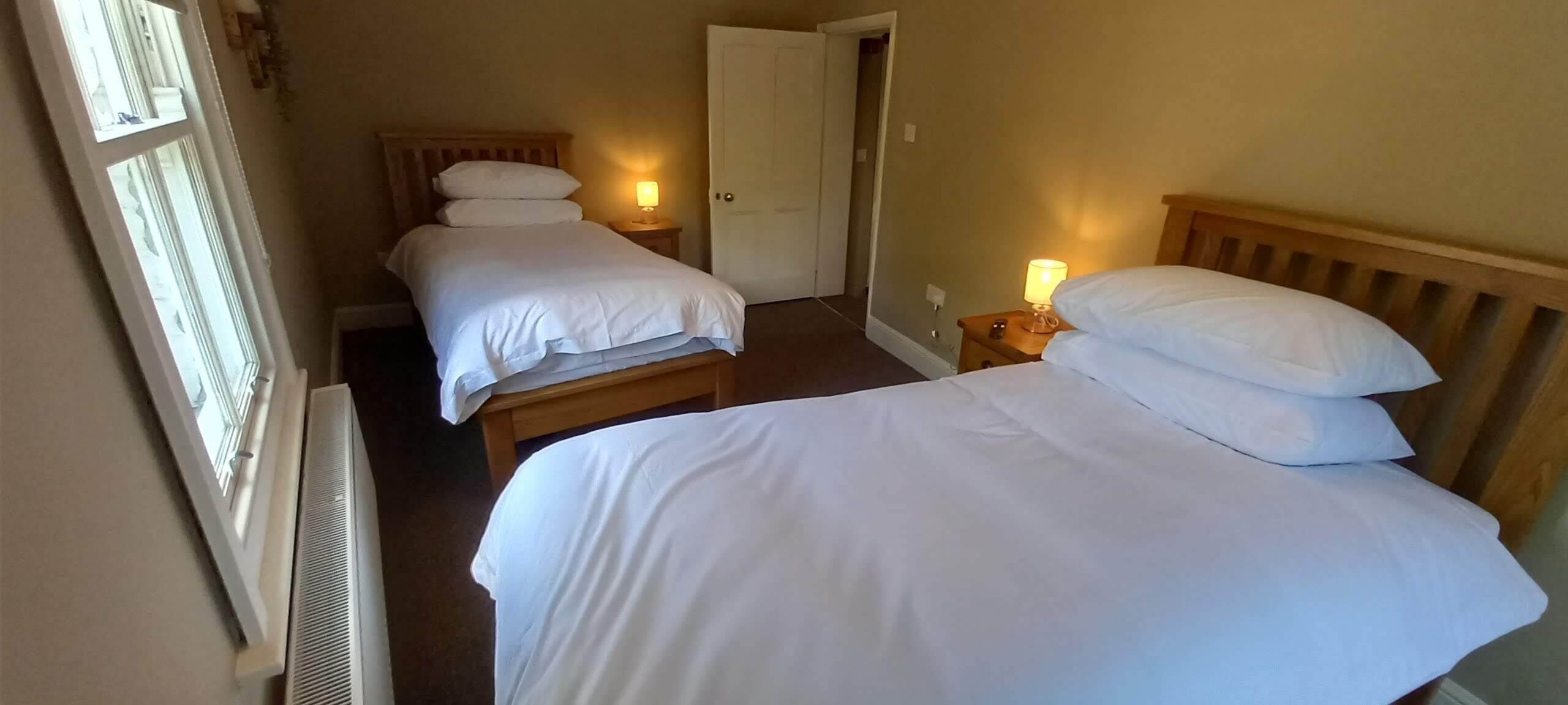 A hotel room with two single beds, each with a bedside table and lamp.