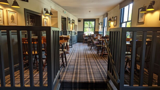 A hotel corridor with checkered carpet, wooden chairs, and tables arranged along the walls. - The Buck Hotel (Middlesbrough)