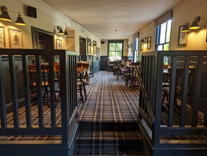 A hotel corridor with checkered carpet, wooden chairs, and tables arranged along the walls. - The Buck Hotel (Middlesbrough)
