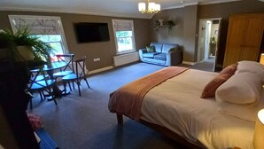 A bedroom with a bed, bedside table, lamp, and a view of a dining area with a table and chairs. - The Buck Hotel (Middlesbrough)