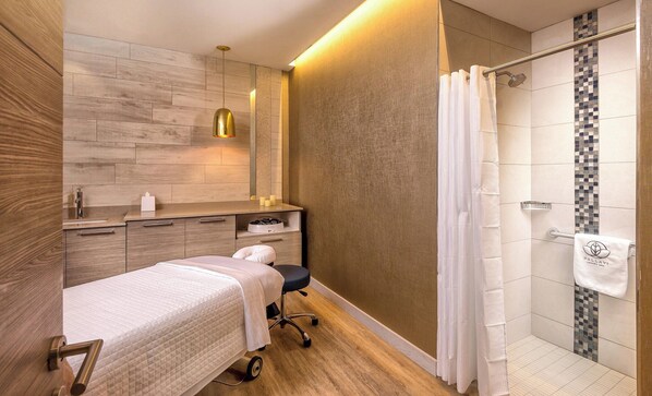 A modern bathroom with a wooden vanity, a shower with a glass door, and a bed with a white bedspread.