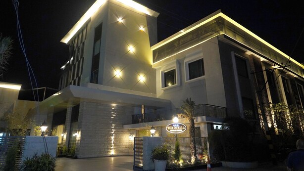 Un hotel moderno con una entrada bien iluminada, un cartel anunciador y un área ajardinada con plantas.
