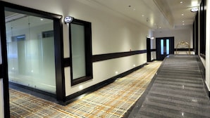 Un pasillo de hotel con alfombra estampada, un mostrador de recepción y una entrada con puerta de vidrio.