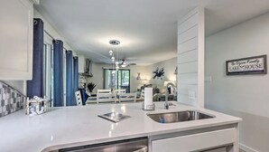 Una cocina moderna con una isla central, pileta de acero inoxidable y mobiliario blanco. En la pared hay un cartel que dice "The Dycon Family Lake House".