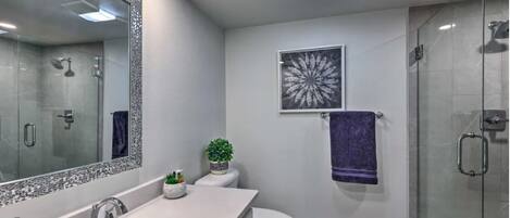 Un baño moderno con un espejo grande, un lavabo, un inodoro y una ducha.