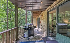 A covered porch with a grill and a fire extinguisher, overlooking a forested area.