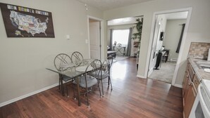 A dining area with a glass table and metal chairs, a kitchen with a sink and cabinets, and a living area with a couch and a coffee table.