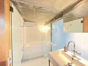 Un baño moderno con cabina de ducha de vidrio, un lavabo blanco con grifo cromado y un espejo sobre el lavabo.