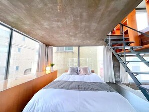 Un dormitorio moderno con una cama grande, vistas a la ciudad y una escalera.