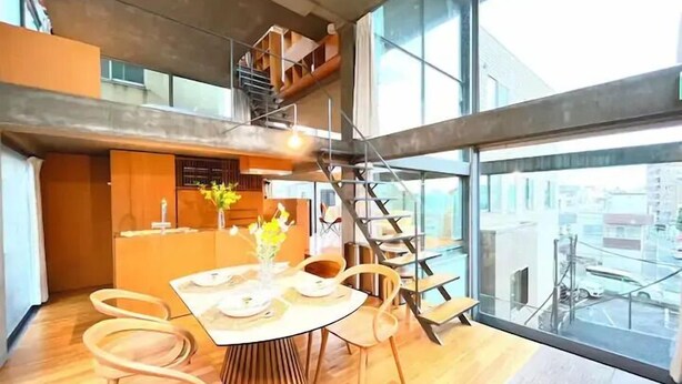 Un comedor moderno con una mesa de madera, sillas y vistas a la ciudad a través de grandes ventanales.