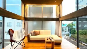 Una sala de estar moderna con un sofá, una silla y una mesita, con ventanas amplias que ofrecen vistas de la ciudad.