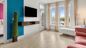 Ein modernes Wohnzimmer mit einem flachbildfernseher an der Wand, einem großen Fenster mit Vorhängen, einem weißen Sofa und einem kleinen Tisch mit einer Lampe.