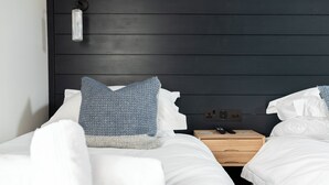 Une chambre d’hôtel moderne avec une tête de lit en bois foncé, du linge de lit blanc et une table de chevet en bois sur laquelle se trouvent un téléphone et une télécommande.