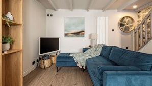Un salon moderne avec un canapé bleu, des étagères en bois, un téléviseur à écran plat et un tableau accroché au mur.