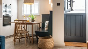 Une cuisine avec des chaises en bois, une table, un panier en osier et une fenêtre avec des stores.