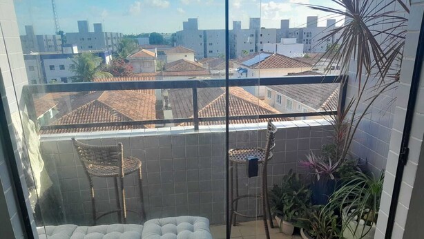 A balcony with two cushioned seating areas, a wicker chair, and potted plants. - 3-bedroom apartment in wonderful João Pessoa with AC, fitness room (José Américo de Almeida João Pessoa)