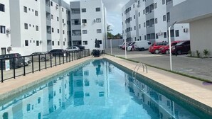 A swimming pool with tiled flooring, surrounded by a black fence. - 3-bedroom apartment in wonderful João Pessoa with AC, fitness room (José Américo de Almeida João Pessoa)