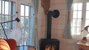 Een gezellige kamer met houten inrichting, een open haard, een raam met gordijnen en een kamerbreed tapijt met dessin.