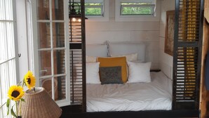Een kamer met een bed, een houten tafel, een stoel, een raam met zonwering en een wandplank.