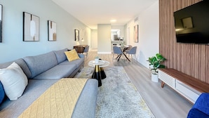 Ein modernes Wohnzimmer mit einem grauen Sofa, einem Couchtisch und einem an der Wand befestigten Fernseher.