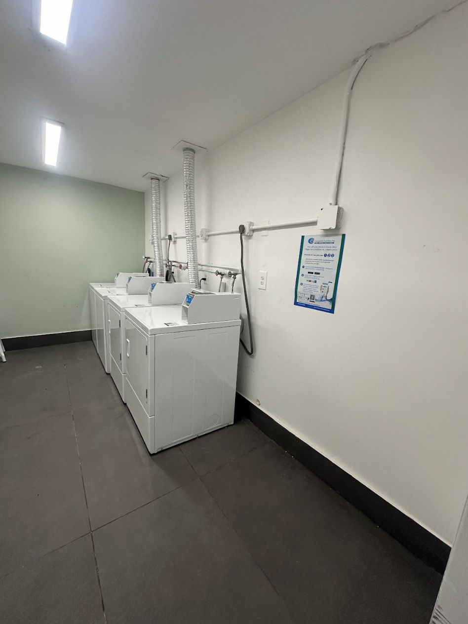 A laundry room with multiple washers and dryers, a ventilation system, and a posted sign on the wall.