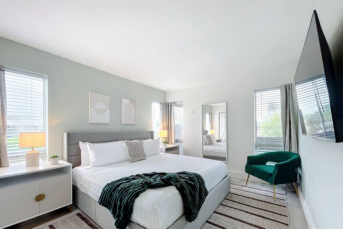 Un dormitorio moderno con una cama grande, mesitas de noche, un espejo y una silla verde.