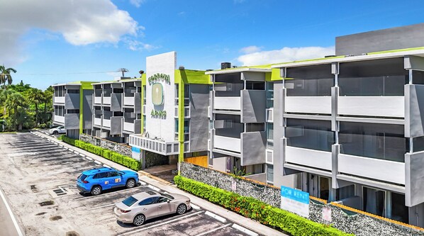 A modern building with a green and white facade, labeled 'GORDON ARMS'. It features a parking lot with several cars, including a blue SUV and a silver sedan.