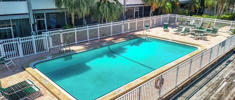 A rectangular pool with a white fence and lounge chairs.