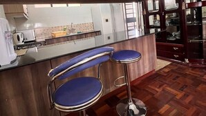 A kitchen with wooden cabinets, a countertop, and a bar area with three blue bar stools. - Cosy Nairobi 1bdr Apartment for Two in Westlands (Nairobi)