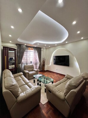 A modern living room with leather sofas, a glass coffee table, and a flat-screen TV mounted on a curved wall. - Cosy Nairobi 1bdr Apartment for Two in Westlands (Nairobi)
