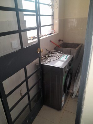 A laundry room with a washing machine, a drying rack, and a window with blinds. - Cosy Nairobi 1bdr Apartment for Two in Westlands (Nairobi)