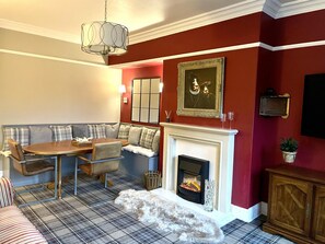 A dining area with a wooden table and bench, a fireplace, and a plaid-patterned rug.