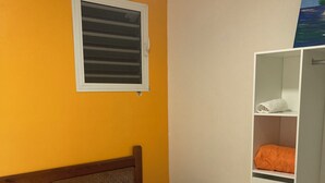 A hotel room with two beds, a wooden headboard, a small wooden table, a white wardrobe, and a window with blinds.